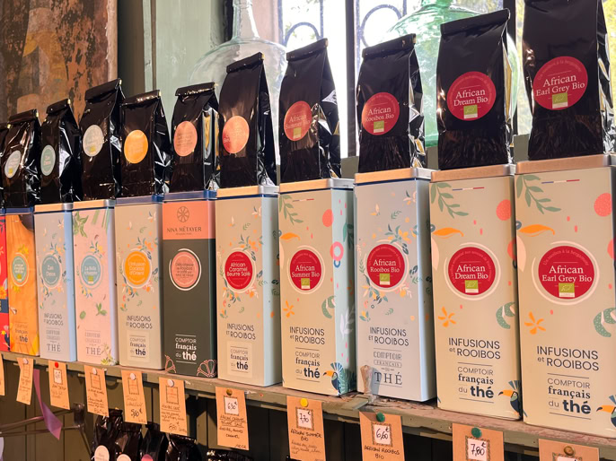 Boîtes de thé rouges alignées sur une étagère, avec des étiquettes colorées et des motifs étoilés.