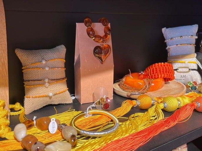 Bijoux colorés exposés sur une étagère, comprenant des colliers, bracelets et perles dans des tons jaunes, oranges et rouges.