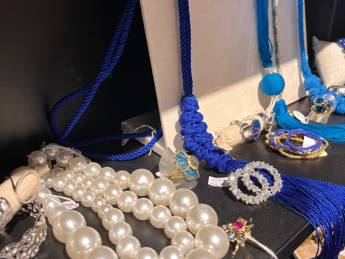 Bijoux exposés, comprenant des colliers de perles blanches et bleues, des bracelets et des broches sur une étagère.