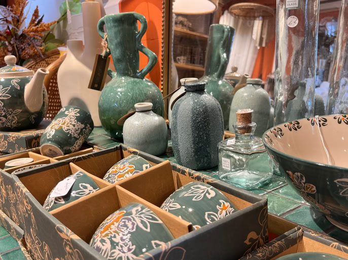 Objets en céramique verte avec motifs floraux, comprenant des théières, des vases, des bols et des boîtes, exposés sur une table.