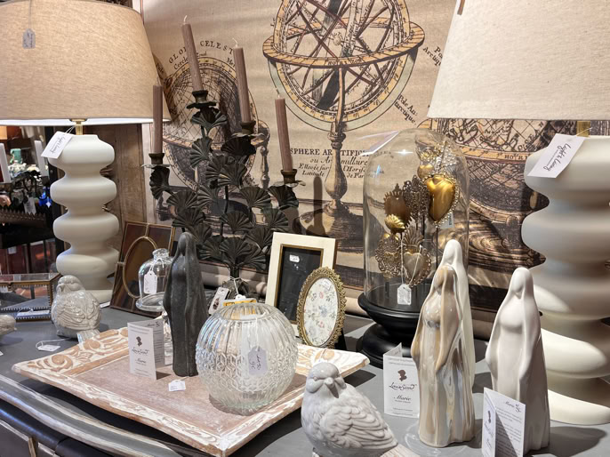 Table avec divers objets décoratifs, y compris des lampes, des sculptures, des vases et des cadres, sur fond de tableau artistique.