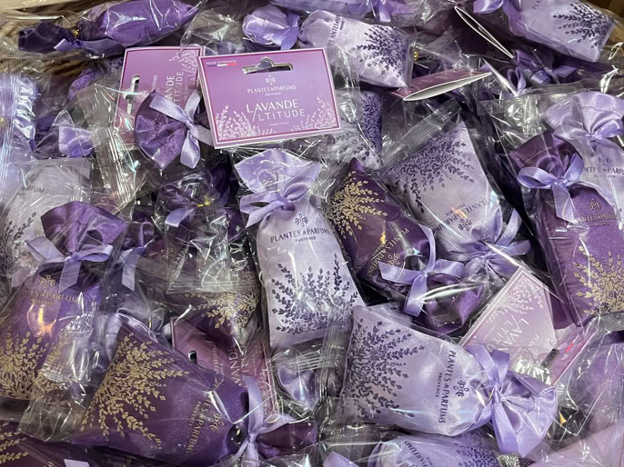 Des sachets violets remplis de lavande, décorés de motifs dorés et attachés avec des rubans, sont empilés dans un panier.