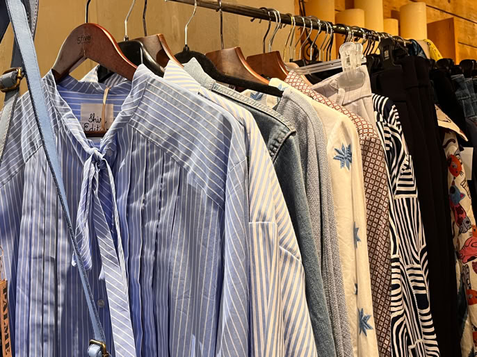 Vêtements suspendus sur un portant, comprenant des chemises à rayures bleues et blanches, et d'autres vêtements de différentes couleurs et motifs.