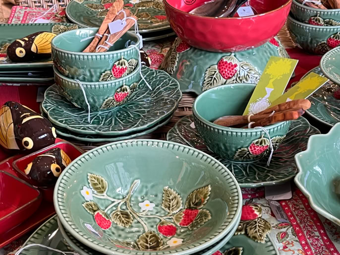 Vaisselle en céramique verte avec motifs de fraises, comprenant des bols, des assiettes et des tasses, disposée sur une nappe rouge.