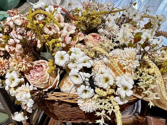 Un panier rempli de fleurs séchées de différentes couleurs, principalement blanches et roses, avec des éléments verts et jaunes.