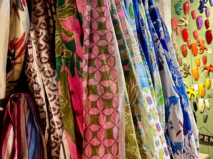 Des tissus colorés suspendus avec des motifs variés, à côté d'un mur décoré de formes colorées et d'une porte verte.
