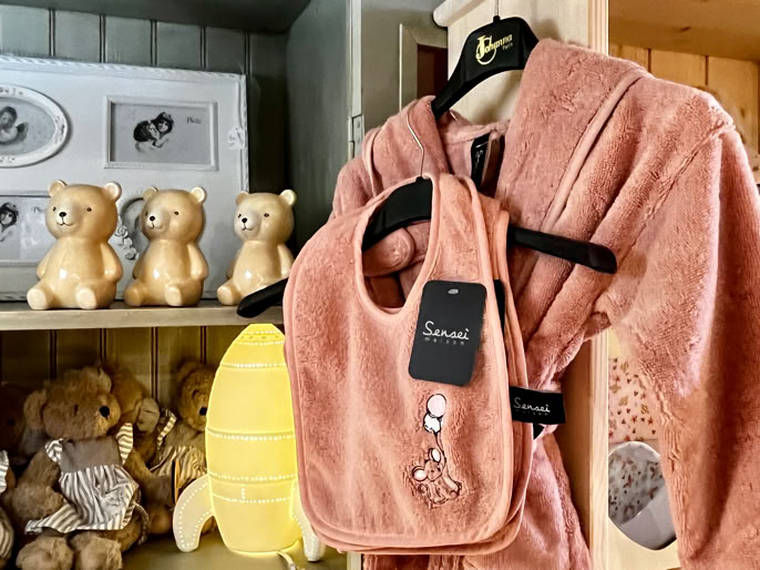 Peignoir rose suspendu avec un bavoir assorti, étagères en arrière-plan contenant des peluches et des cadres photo.