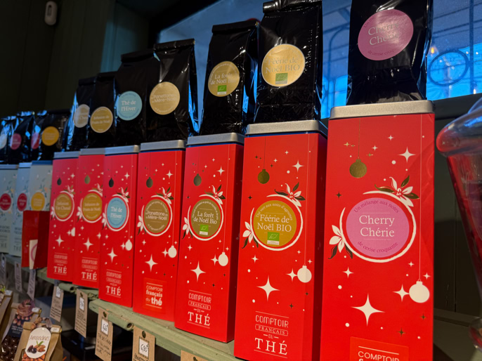 Boîtes de thé rouges alignées sur une étagère, avec des étiquettes colorées et des motifs étoilés.