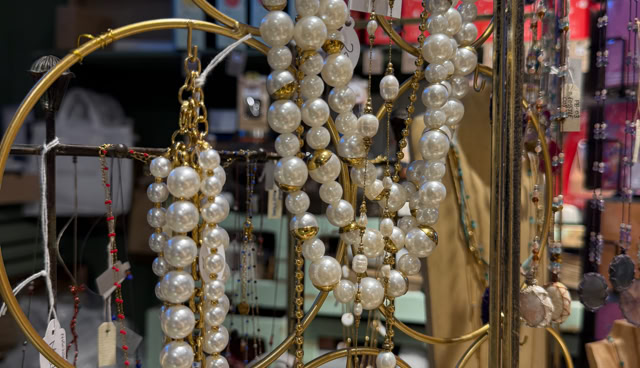 Colliers de perles blanches suspendus à un présentoir doré avec un fond flou de divers objets.