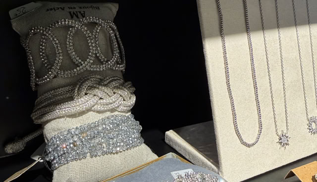 Présentoir de bijoux avec colliers, bracelets et boucles d'oreilles en perles et métal argenté, sur fond noir.