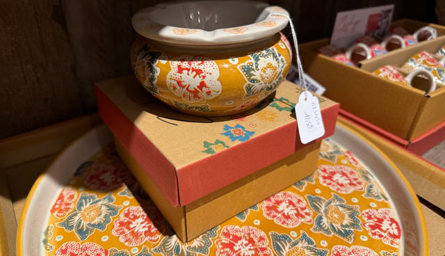 Bol décoratif jaune avec motifs floraux rouges et verts, posé sur une boîte en carton, à côté d'un plateau assorti.