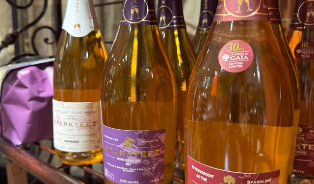 Bouteilles de cidre pétillant sur une étagère en métal, avec des étiquettes colorées et des emballages en carton en dessous.