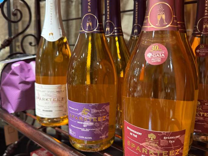 Bouteilles de thé pétillant sur une étagère en métal, avec des étiquettes de différentes couleurs, et des boîtes en carton en dessous.