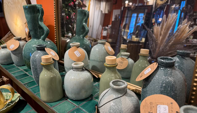 Vases en céramique de différentes formes et tailles sur une étagère, avec des étiquettes attachées, reflétés dans un miroir.