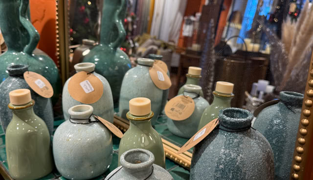 Vases en céramique de différentes formes et tailles sur une table, avec un miroir reflétant un sapin de Noël décoré en arrière-plan.