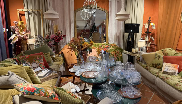 Salon décoré avec des canapés, des coussins colorés, des tables basses avec des verres et des assiettes, des fleurs, des lampes suspendues, et des rideaux.