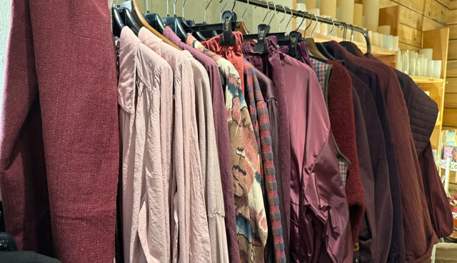 Des chemises de différentes nuances de rouge et rose suspendues sur un portant dans un magasin.