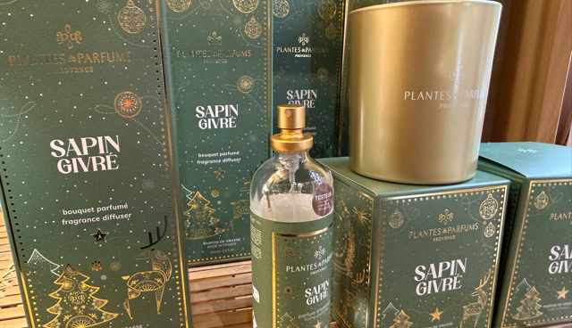 Boîtes vertes et dorées avec des motifs de Noël, une bouteille de parfum et une bougie dorée sur une étagère en bois.