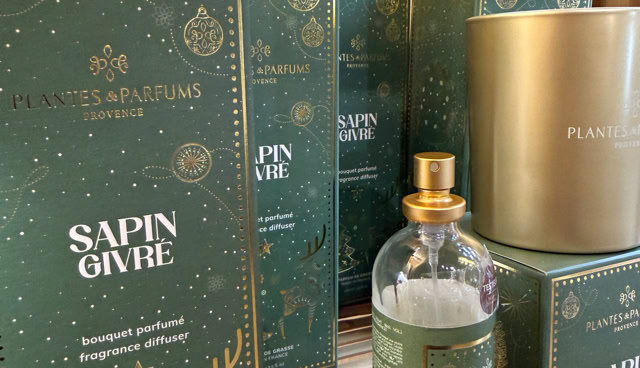 Boîtes vertes et dorées avec des motifs de Noël, une bouteille transparente avec un bouchon doré, posées sur une étagère en bois.