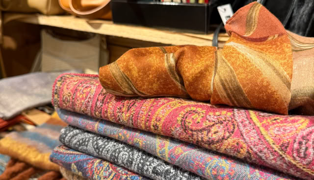 Étagère avec des écharpes colorées pliées, des sacs en cuir et des articles de papeterie.