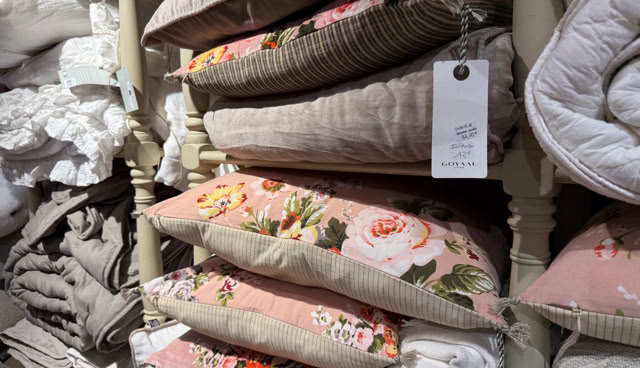 Coussins empilés avec des motifs floraux et étiquettes, entourés de linge de maison.