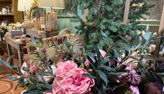 Bouquet de fleurs roses avec des feuilles vertes au premier plan, lampes et objets décoratifs en arrière-plan.