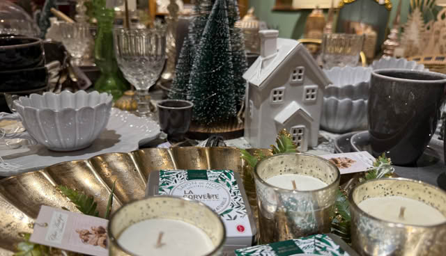 Table décorée avec des bougies, des assiettes, des verres, une maison miniature blanche et un sapin décoratif.