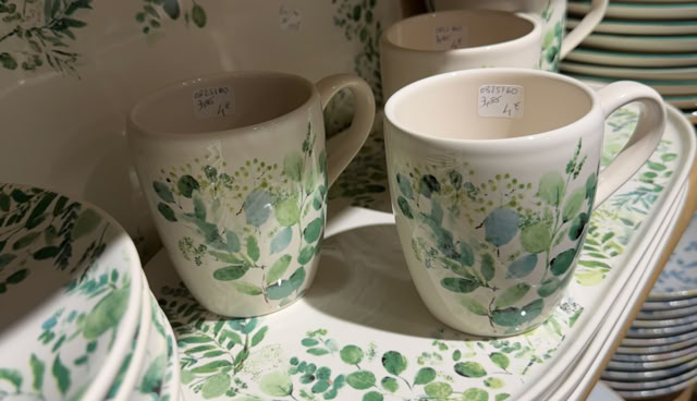 Tasses et assiettes avec motifs floraux verts sur une étagère.