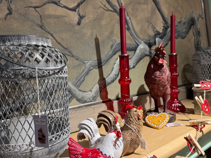 Objets décoratifs sur une étagère, y compris des chandeliers rouges, des figurines de coq, des lanternes en métal et des éléments en bois.