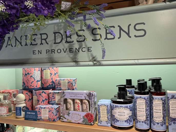 Produits de beauté et soins sur une étagère, avec des emballages décorés de motifs floraux et le texte "Panier des Sens en Provence" en arrière-plan.