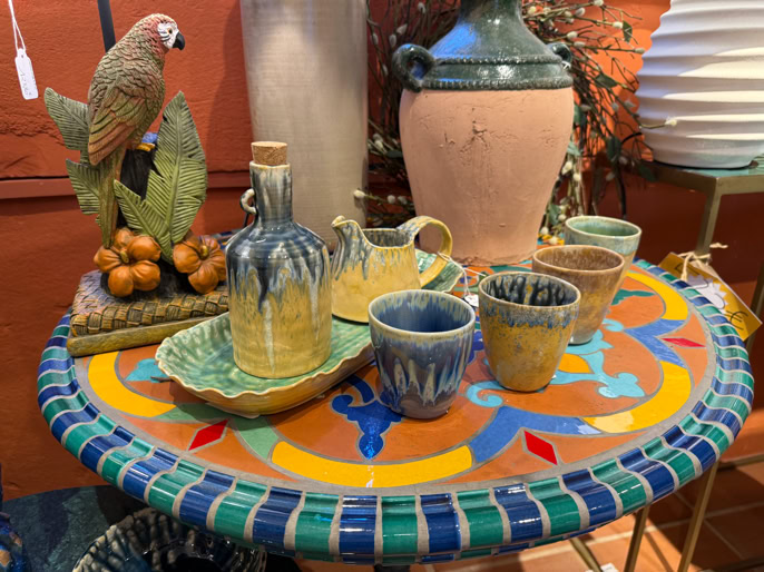 Table ronde colorée avec des objets en céramique, y compris des tasses, des pichets, un plateau, et une statue d'oiseau.