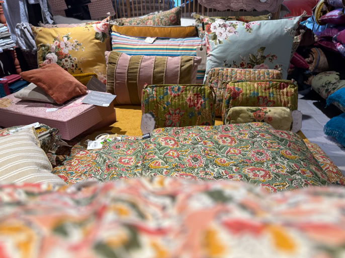 Coussins et oreillers de différentes tailles et motifs floraux empilés sur une surface.