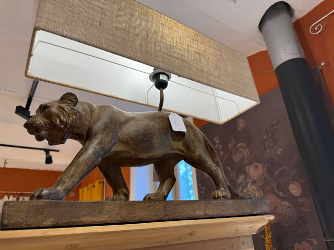 Statue d'un lion en bois sur une étagère, sous une lampe rectangulaire avec un abat-jour en tissu.