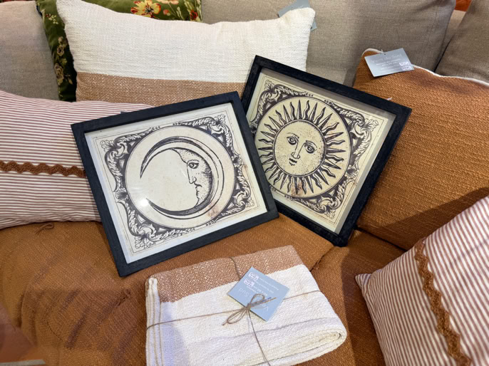 Deux cadres avec des illustrations de la lune et du soleil posés sur des coussins et une couverture pliée.